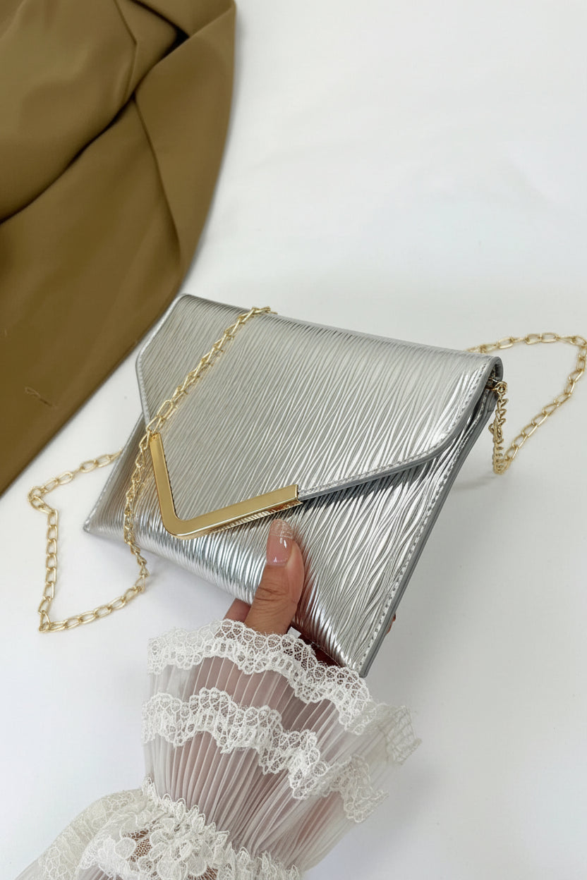Silver clutch with gold chain held by a hand wearing a white lace glove on a white background