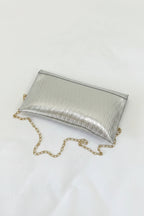 Silver clutch bag with a gold chain on a white surface