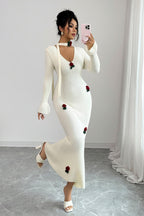 Woman wearing a white dress with red floral embellishments against a plain background