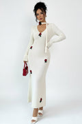 Woman wearing a white dress with red floral embellishments against a plain background
