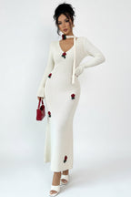 Woman wearing a white dress with red floral embellishments against a plain background