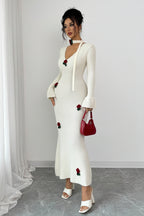 Woman wearing a white dress with red floral embellishments against a plain background