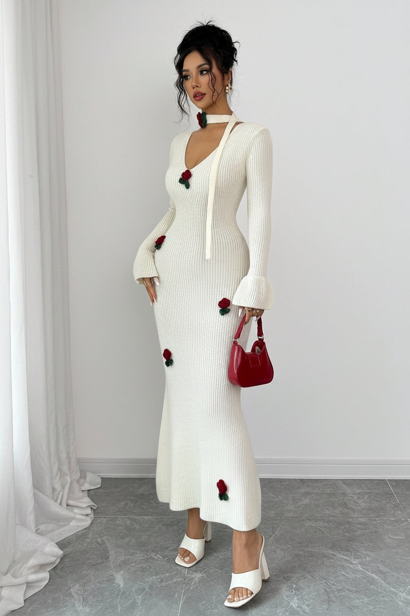 Woman wearing a white dress with red floral embellishments against a plain background