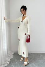 Woman wearing a white dress with red floral embellishments against a plain background