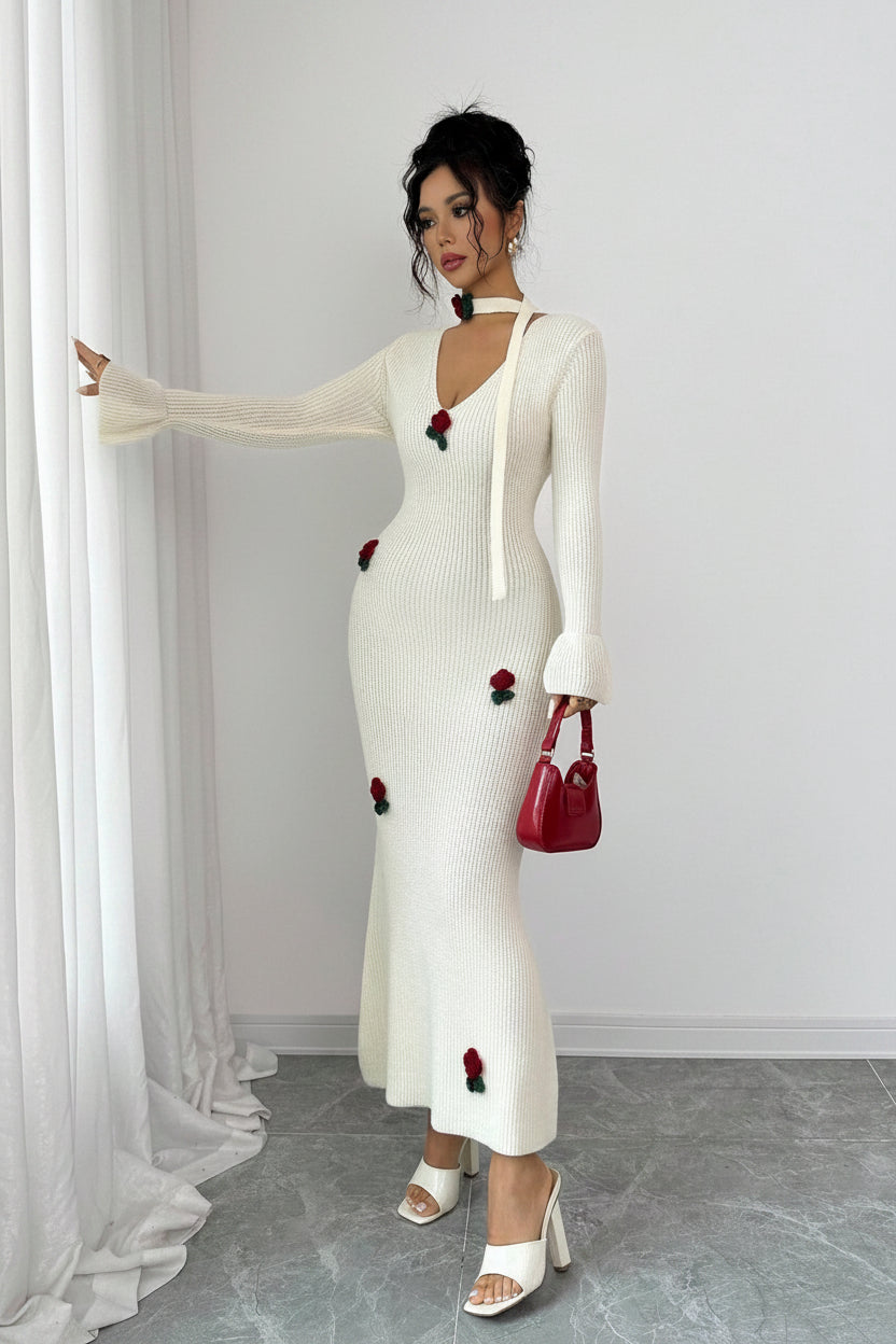 Woman wearing a white dress with red floral embellishments against a plain background