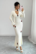 Woman wearing a white dress with red floral embellishments against a plain background