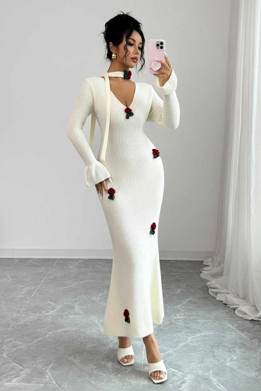 Woman wearing a white dress with red floral embellishments against a plain background