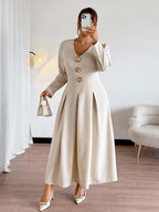 Woman wearing a long beige dress with gold buttons in a room.
