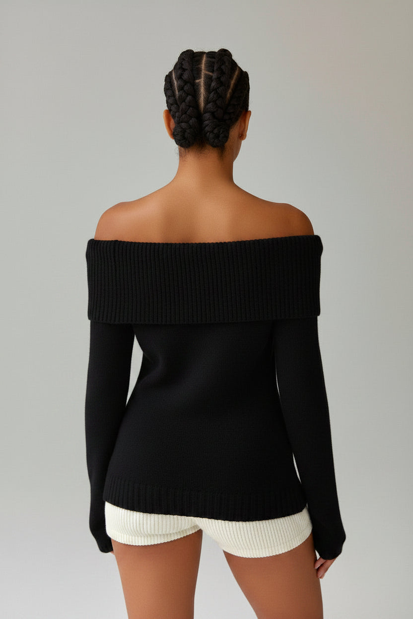 Person wearing a black off-shoulder sweater and white shorts on a plain background