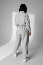 Person wearing a gray tracksuit standing in a minimalistic room with concrete walls and white cabinets.