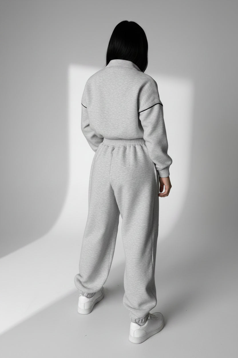 Person wearing a gray tracksuit standing in a minimalistic room with concrete walls and white cabinets.