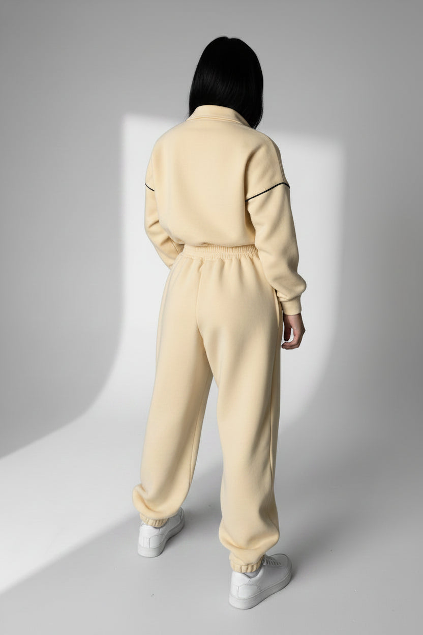 Person wearing a gray tracksuit standing against a white wall.