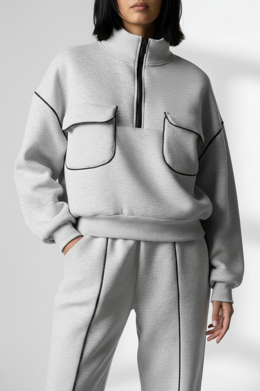 Person wearing a gray tracksuit with black piping against a textured wall.