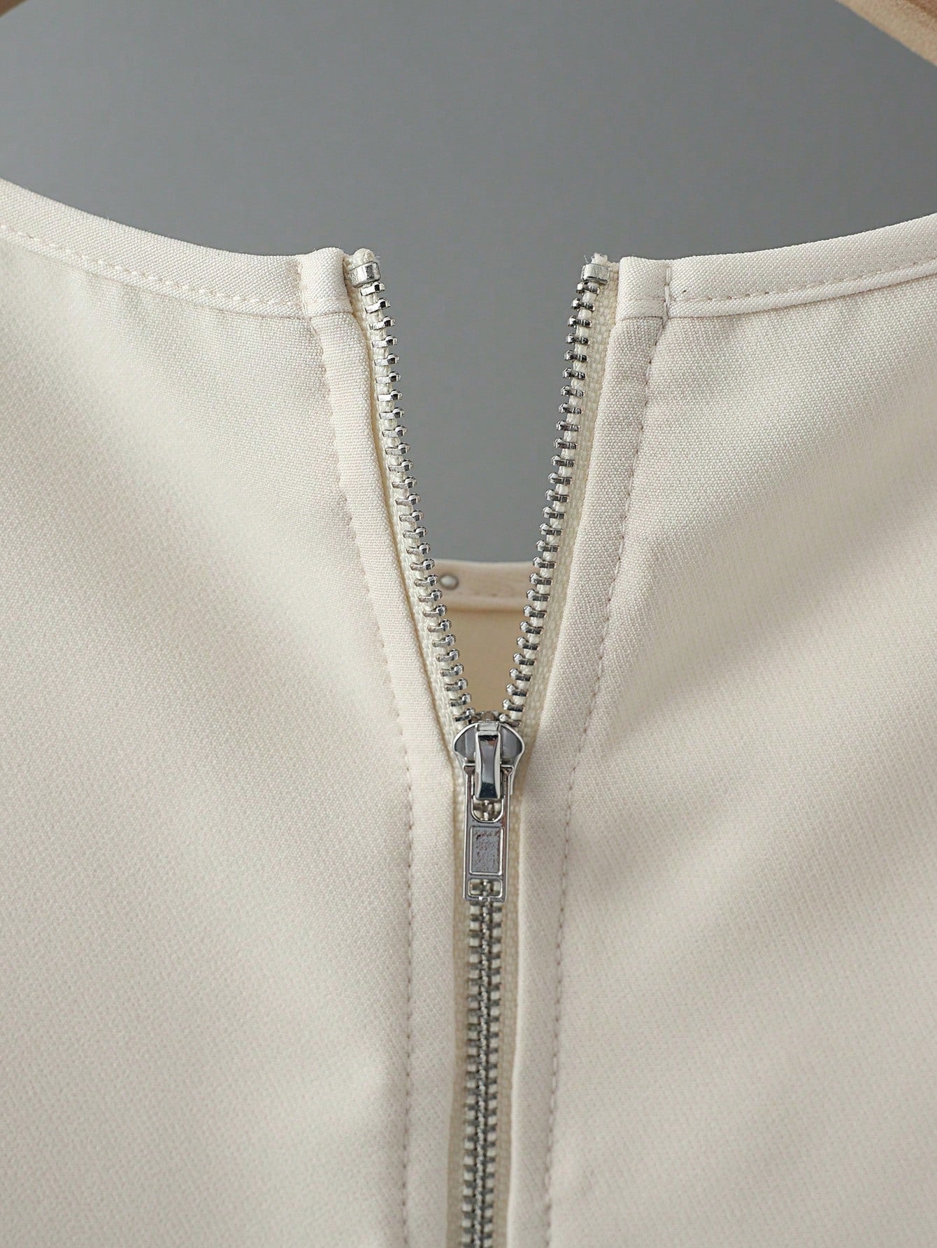 Close-up of a beige jacket with a silver zipper on a gray background