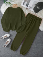 Green sweatshirt and pants set with white sneakers on a gray surface.