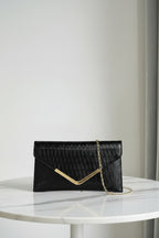 Black clutch bag with gold chain held by a hand against a neutral background, branded 'Chicmod'.