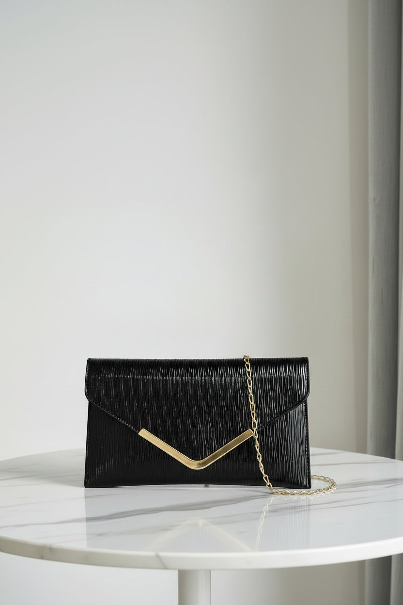 Black clutch bag with gold chain held by a hand against a neutral background, branded 'Chicmod'.