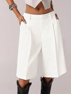 White high-waisted shorts worn with a white top and black boots on a light gray background