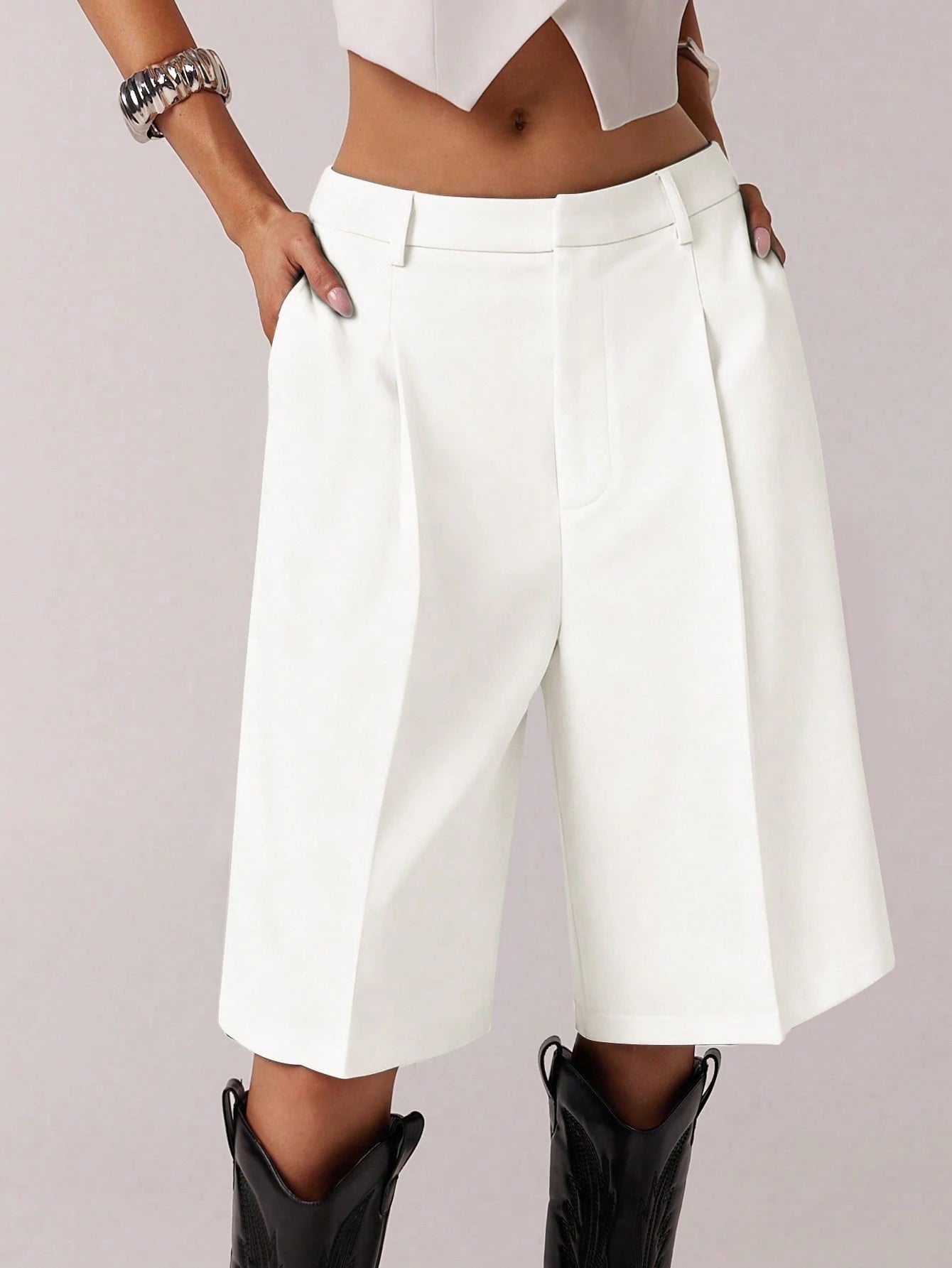 White high-waisted shorts worn with a white top and black boots on a light gray background