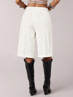 Person wearing white high-waisted shorts and black knee-high boots on a light gray background