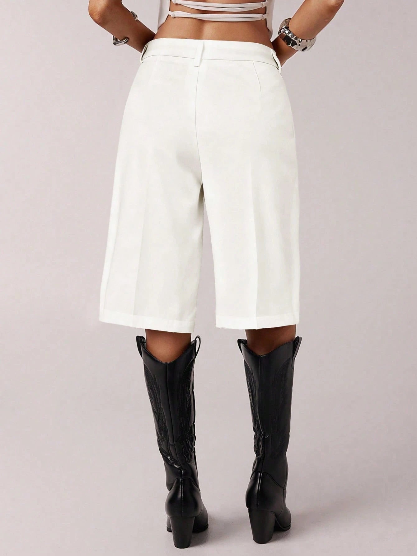 Person wearing white high-waisted shorts and black knee-high boots on a light gray background