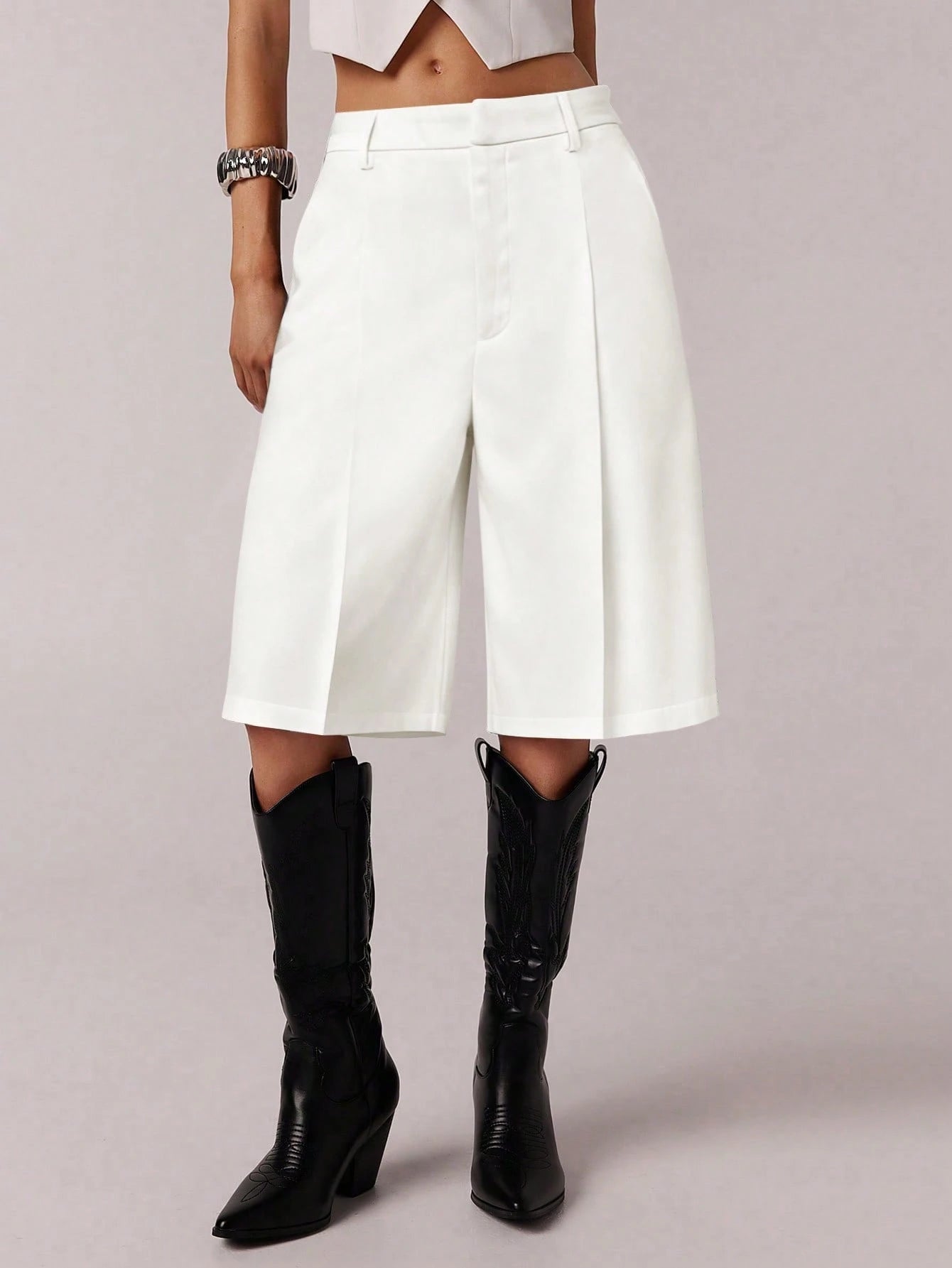 Person wearing white high-waisted shorts and black knee-high boots on a plain background