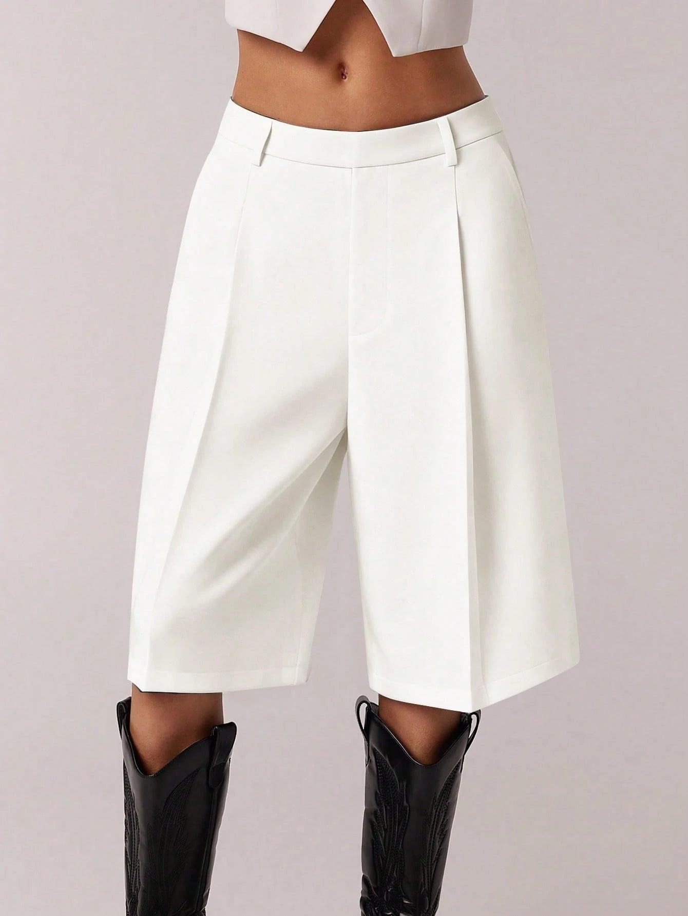 White high-waisted pants worn with black boots on a light gray background
