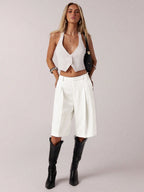 Woman wearing a white sleeveless top, white high-waisted pants, and black knee-high boots on a plain background.