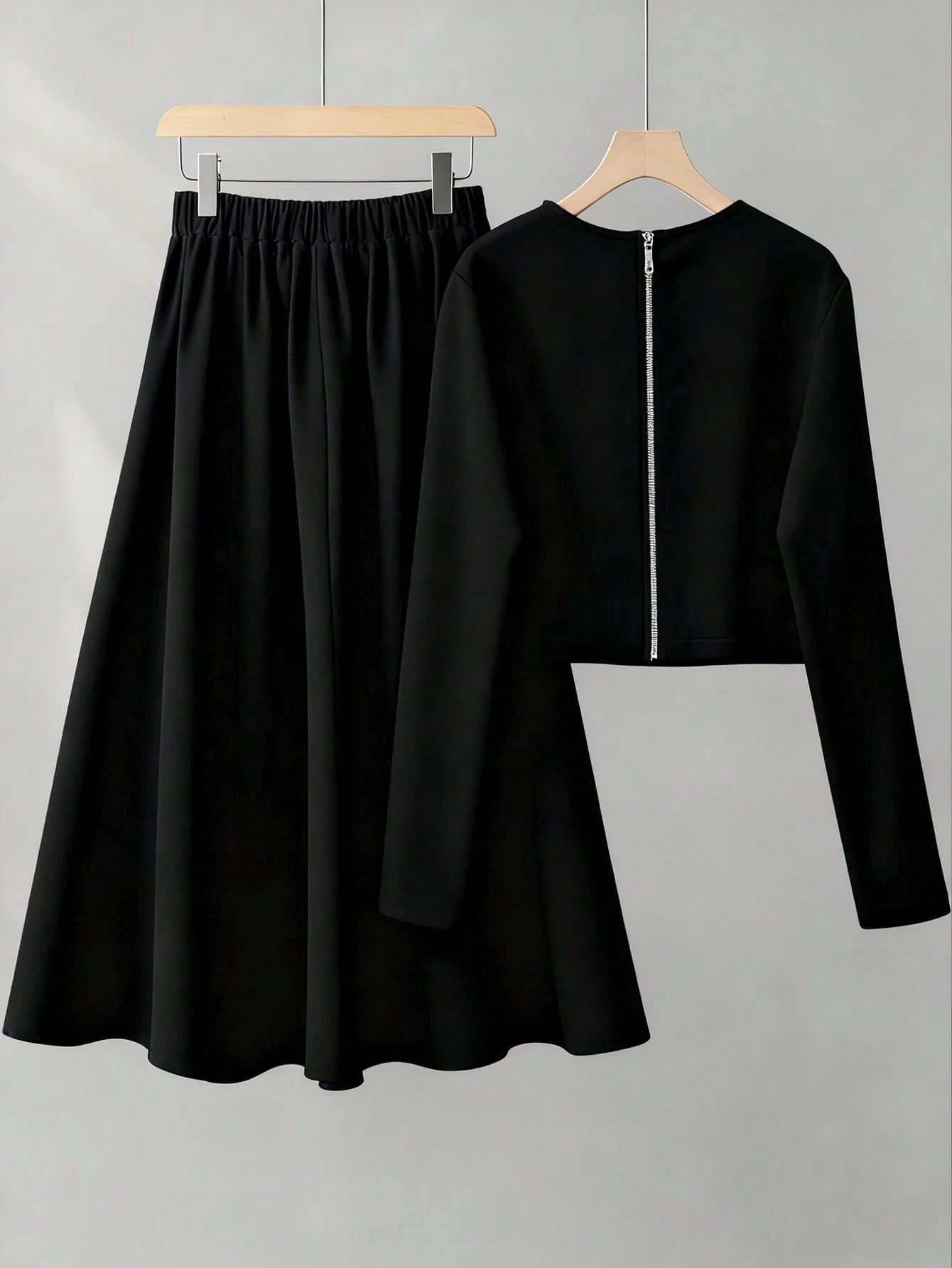 Black long-sleeve top and skirt set on hangers against a gray background