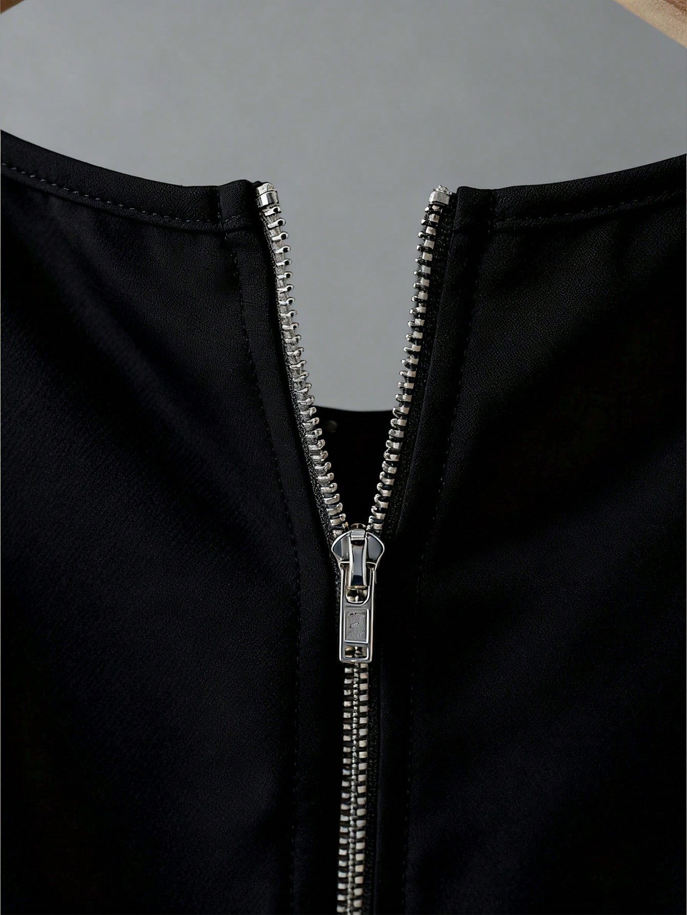 Close-up of a black garment with a silver zipper on a gray background