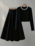 Black outfit with long-sleeve top and skirt on a hanger against a gray background