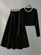 Black outfit with long-sleeve top and skirt on a hanger against a gray background