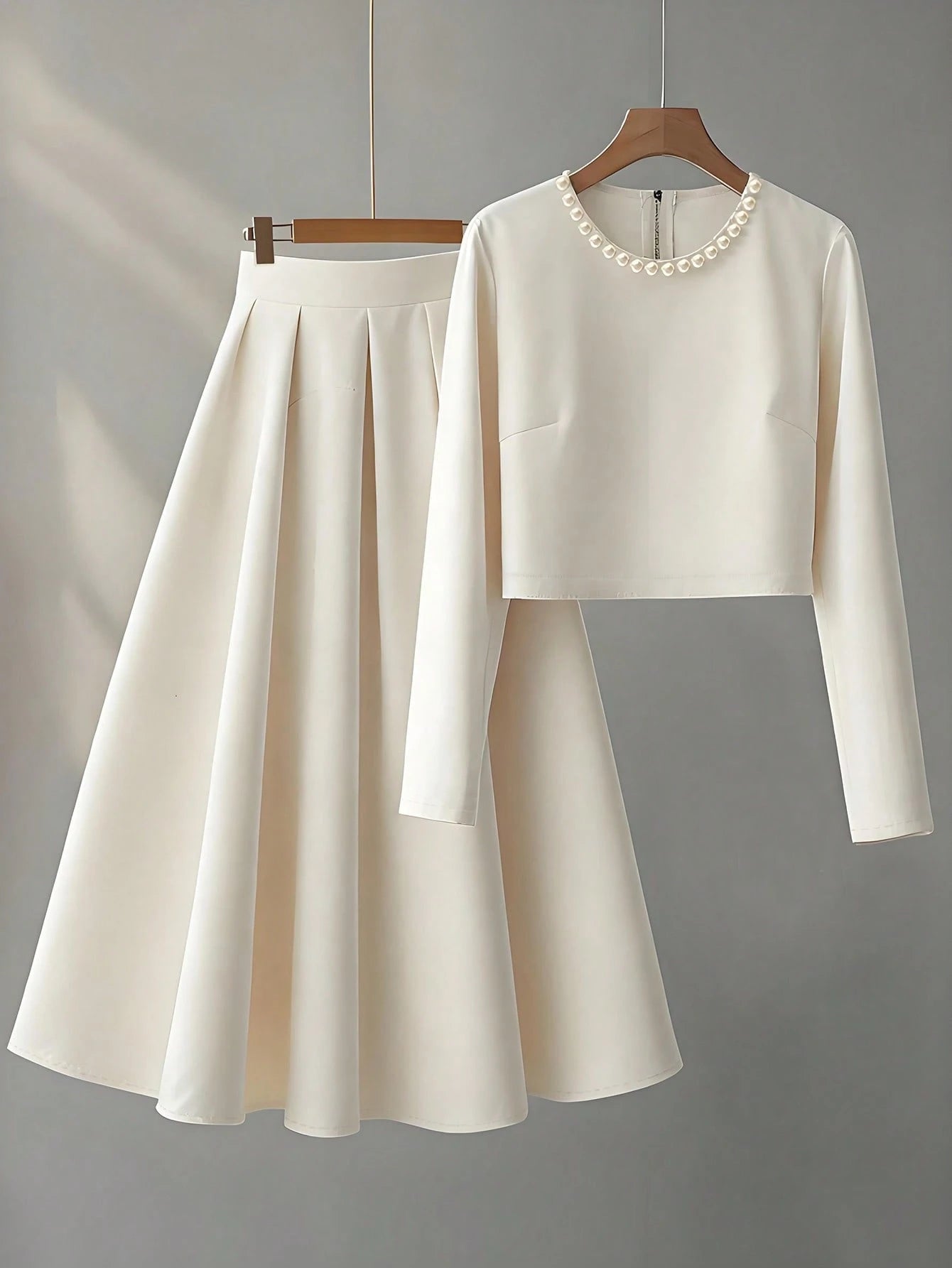 White long-sleeve top and skirt set on hangers against a gray background