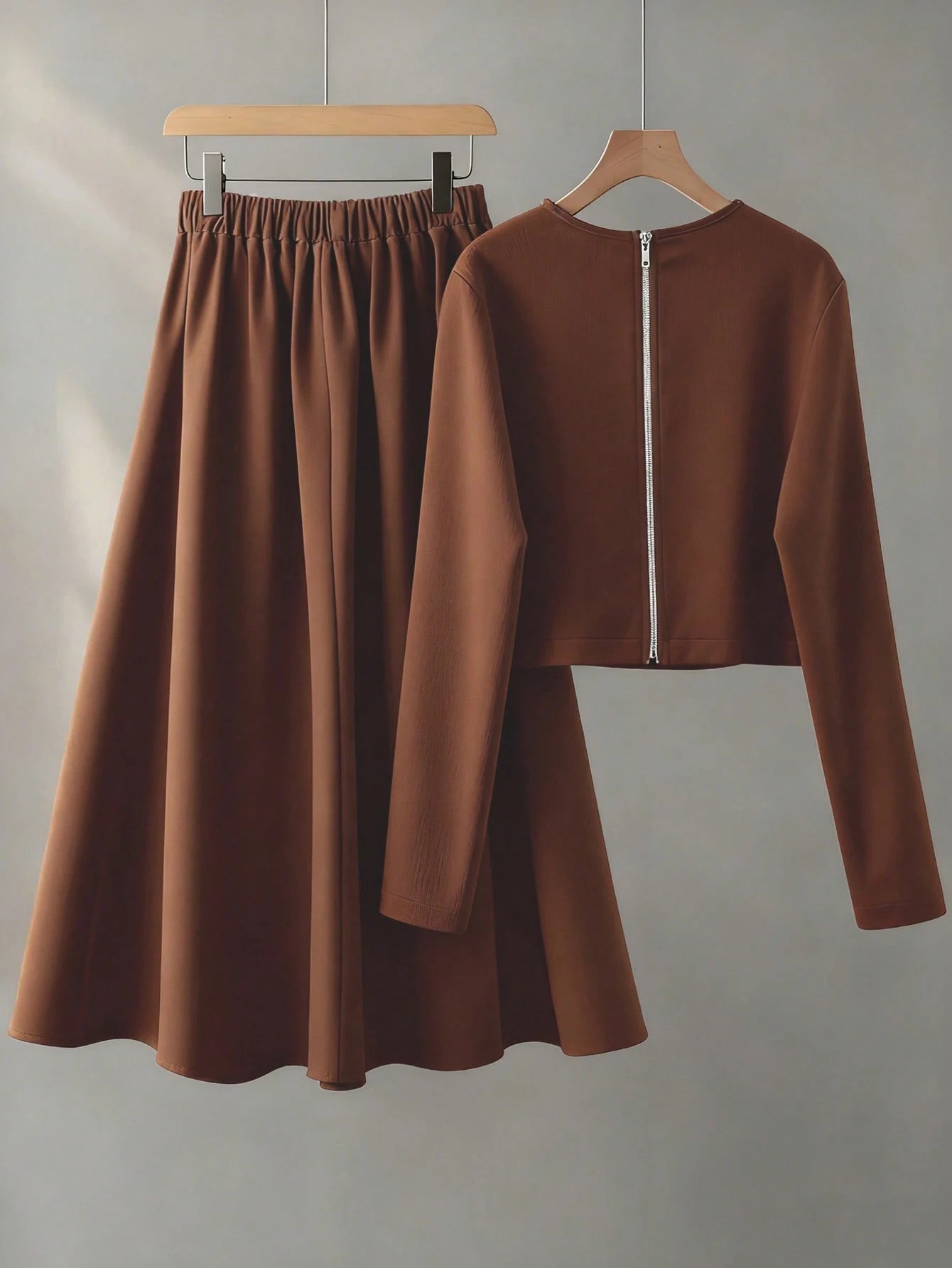 Brown long-sleeve top and skirt set on hangers against a gray background