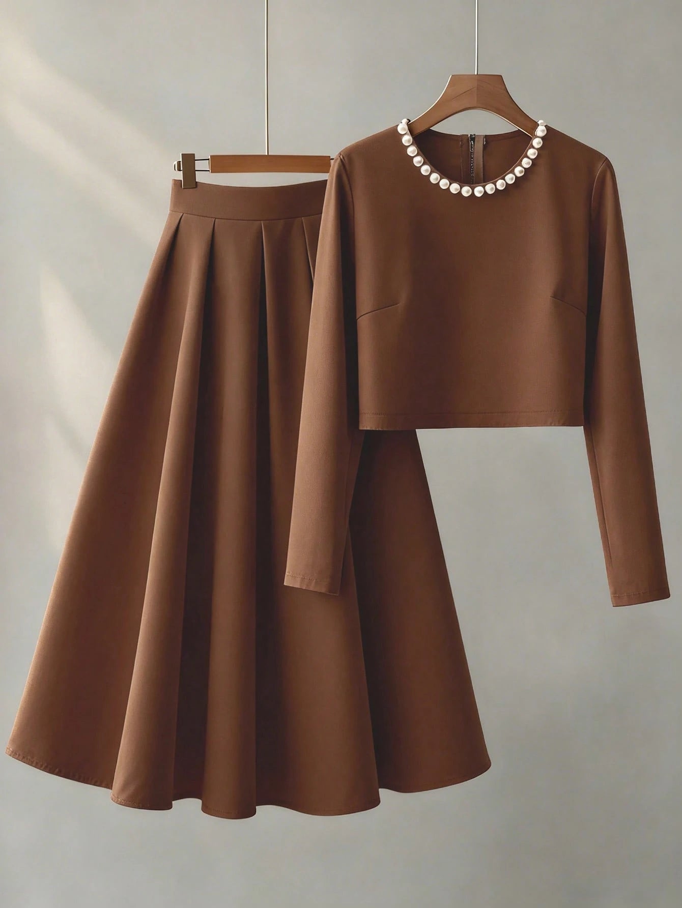 Brown long-sleeve top and skirt set on hangers against a neutral background