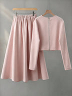 Pink outfit with skirt and long-sleeve top on hangers against a gray background