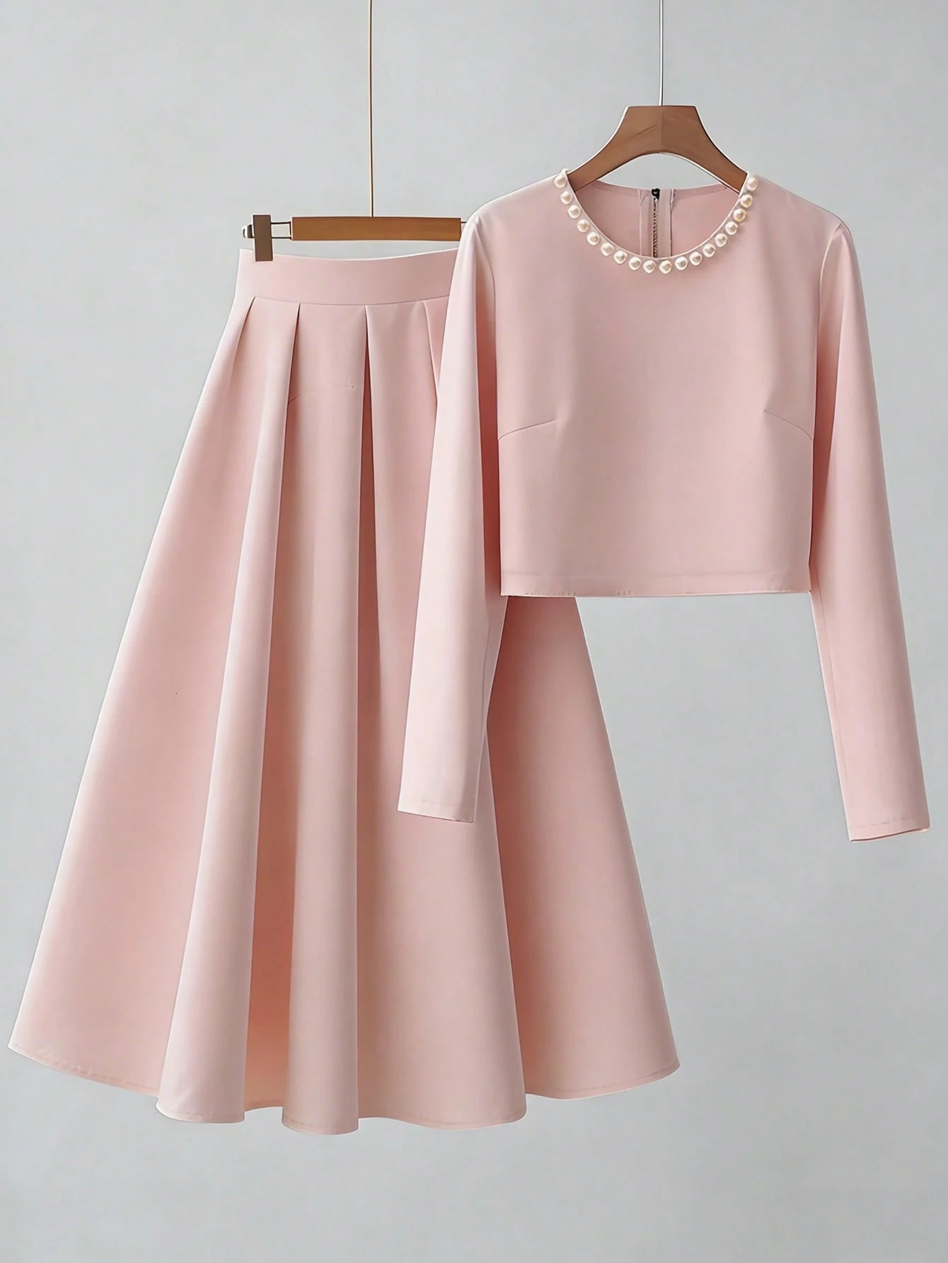 Pink outfit with long-sleeve top and skirt on a hanger against a light gray background