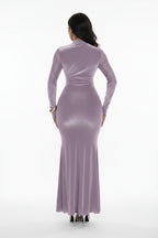 Person wearing a long-sleeve, glittery purple dress against a white curtain background