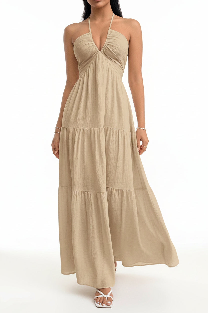 Woman wearing a beige halter neck dress against a white wall.