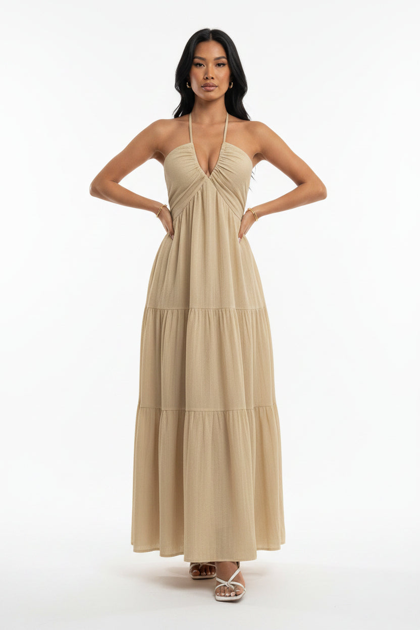Woman wearing a beige halter neck dress against a white wall.