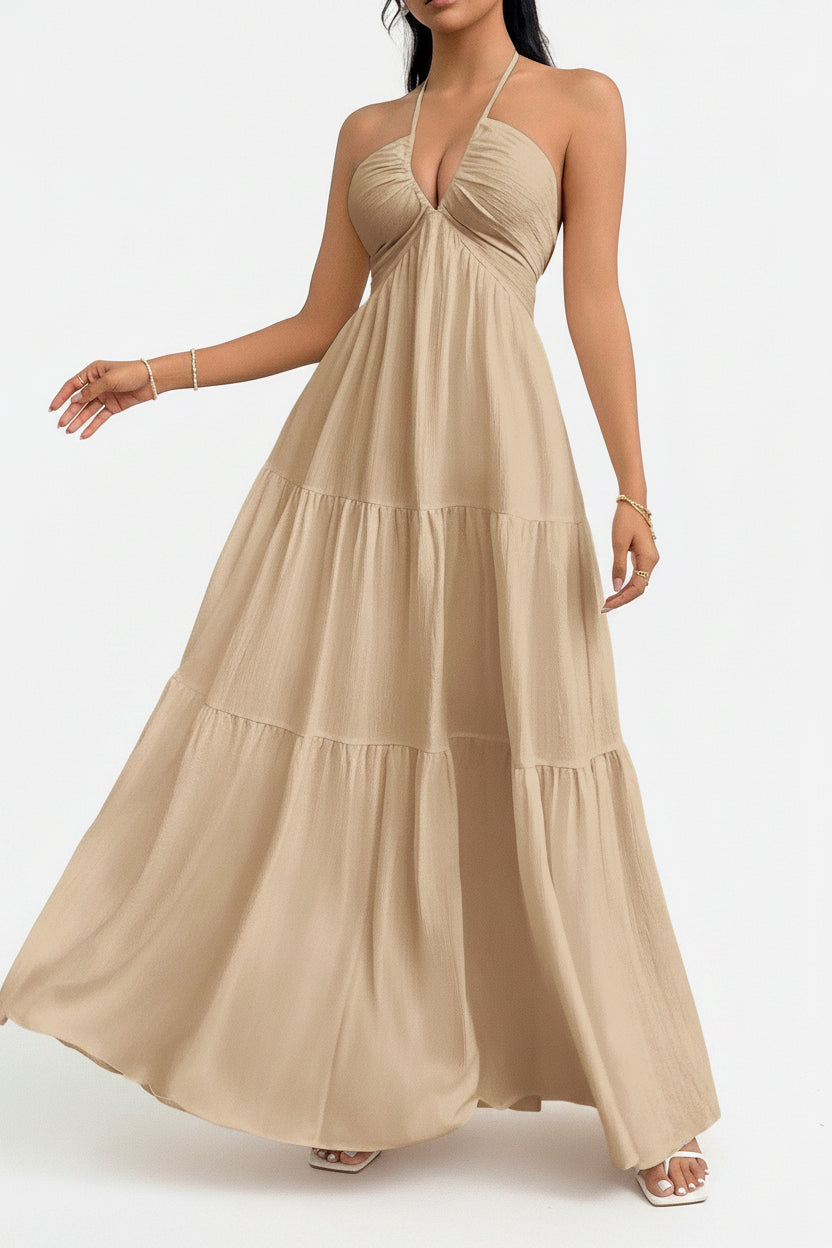 Woman wearing a beige halter neck dress against a white brick wall.