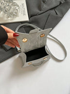 Gray handbag with gold accents held by a hand on a white surface.