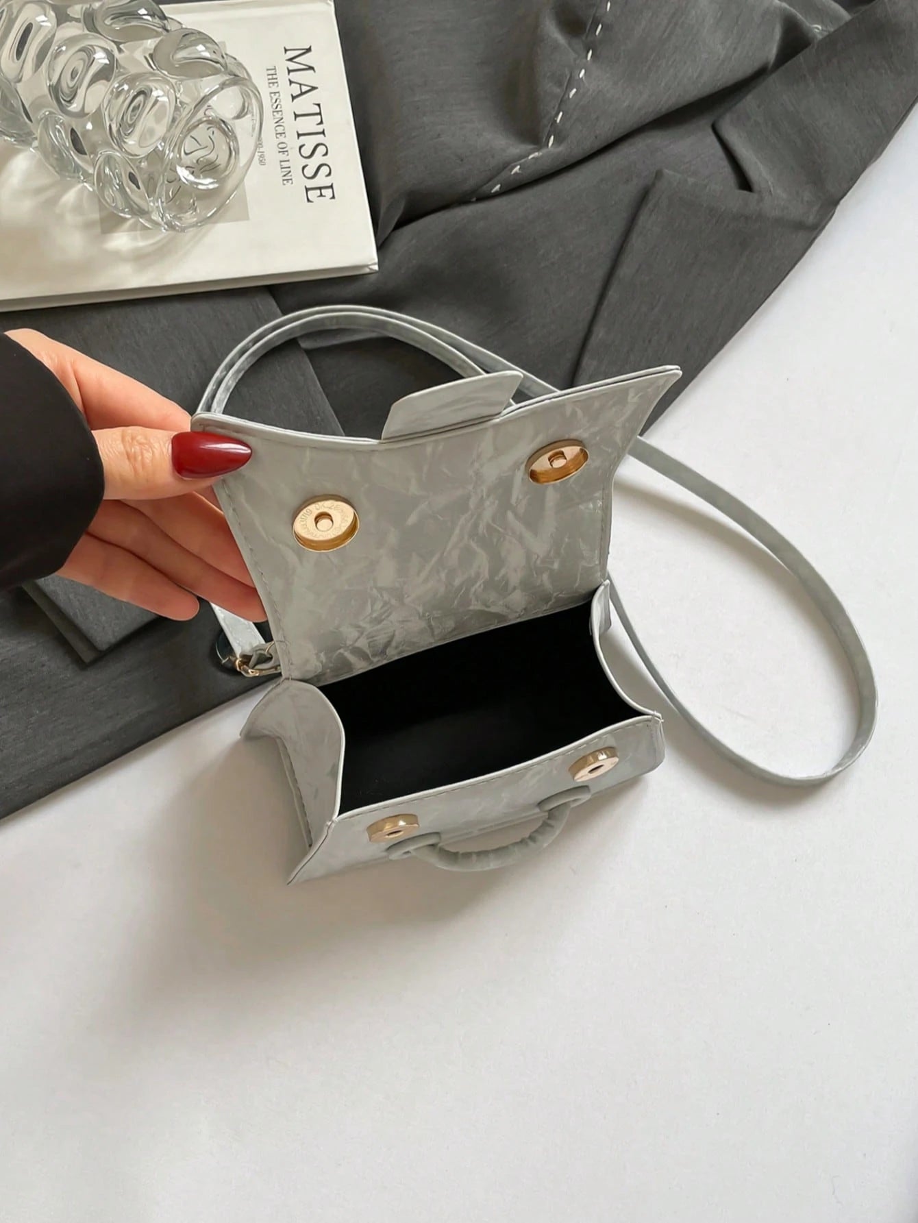 Gray handbag with gold accents held by a hand on a white surface.