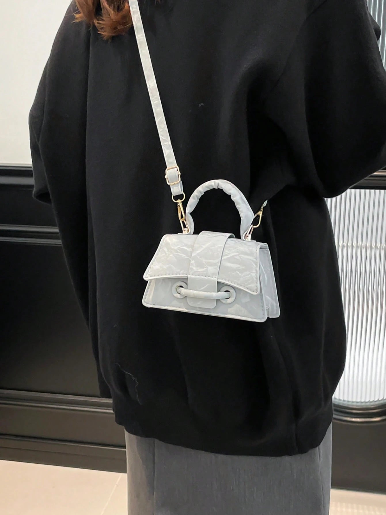 Person wearing a black outfit with a white textured handbag on a neutral background