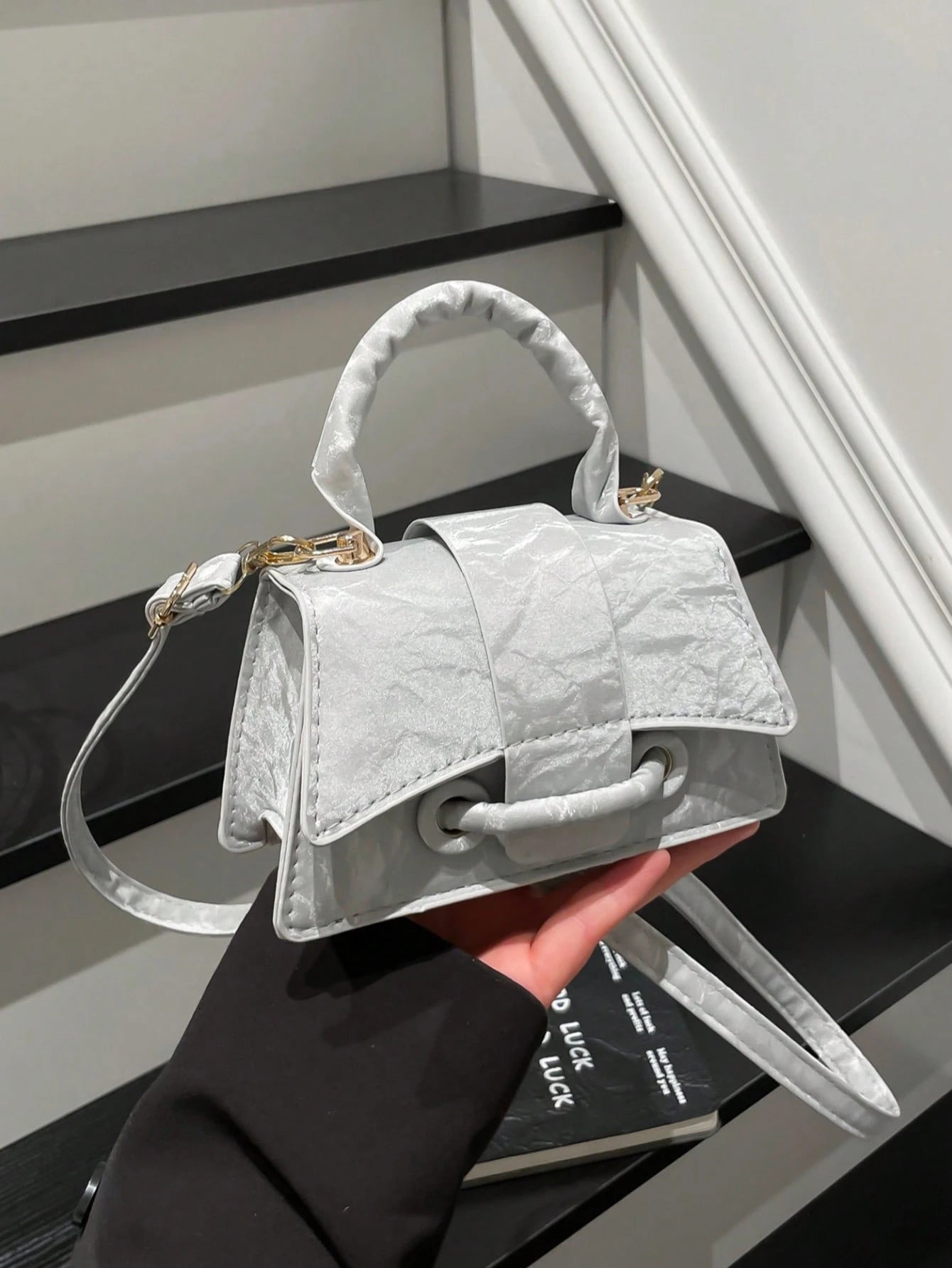 White handbag held by a hand on a staircase
