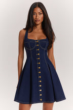 Woman wearing a blue denim dress with gold buttons on a white background
