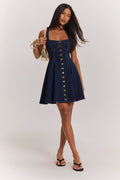Woman wearing a navy denim dress with gold buttons on a white background