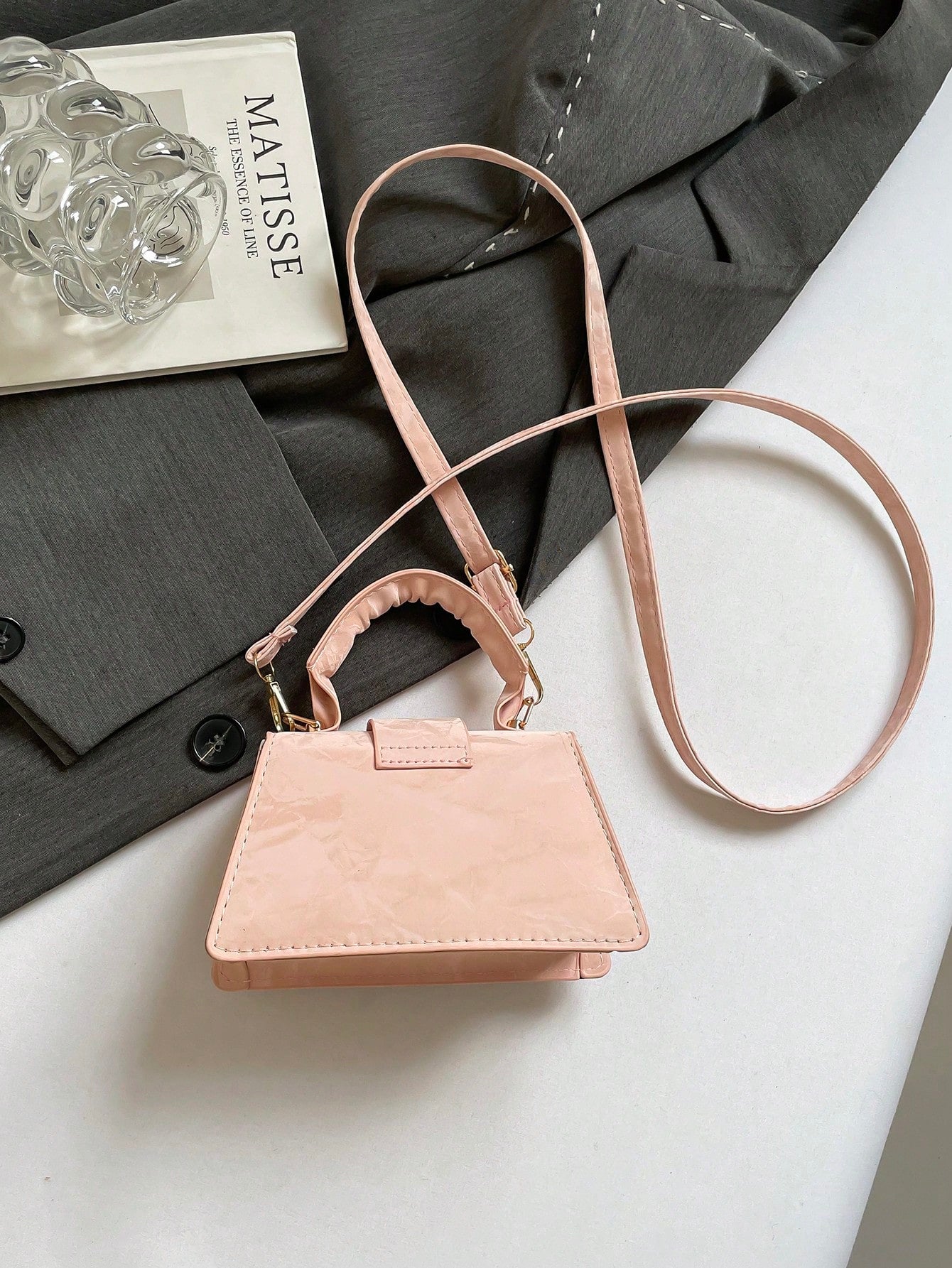 Pink handbag on a white surface with a magazine and gray fabric in the background