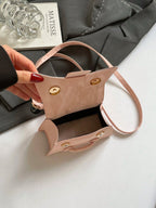 Beige handbag held by a hand with red nail polish on a light gray background