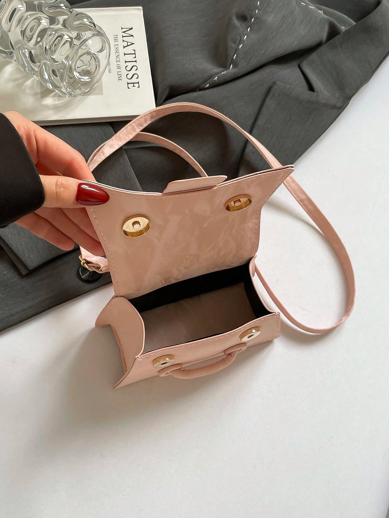 Beige handbag held by a hand with red nail polish on a light gray background